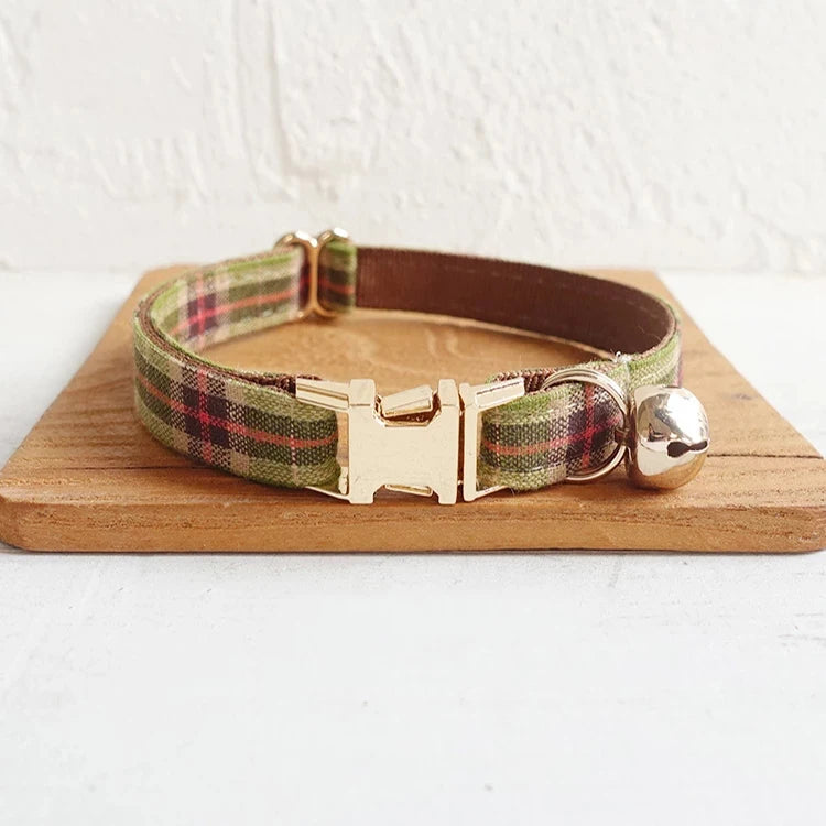 Green and red checkered plaid dog collar with gold buckle and bell on a wooden board