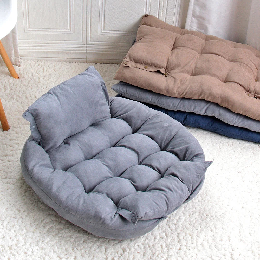 A gray cushioned pet bed arranged in sofa style with stacked beige and navy versions in the background.