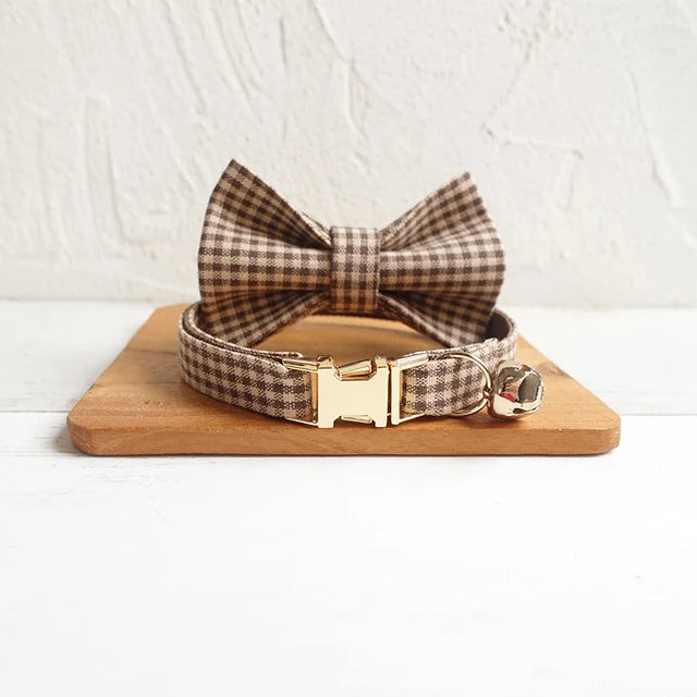Brown gingham plaid dog collar with detachable bow tie and gold buckle on wooden display.