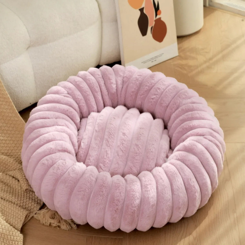 Lilac pet bed on a wooden floor with a beige couch in the background
