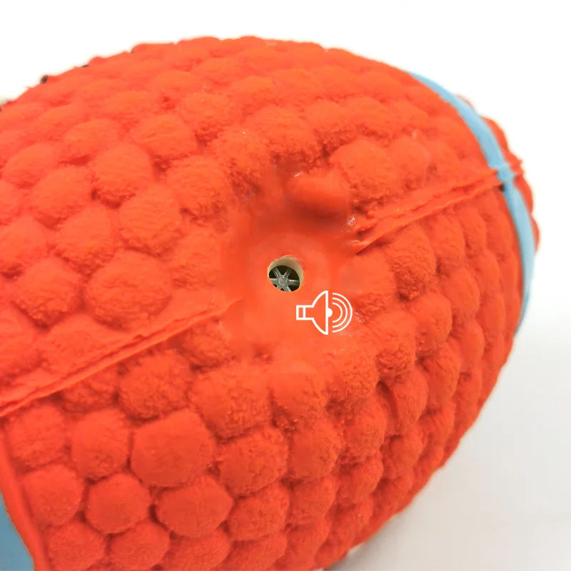 Close-up of an orange plush football toy with a built-in squeaker hole visible in the center.
