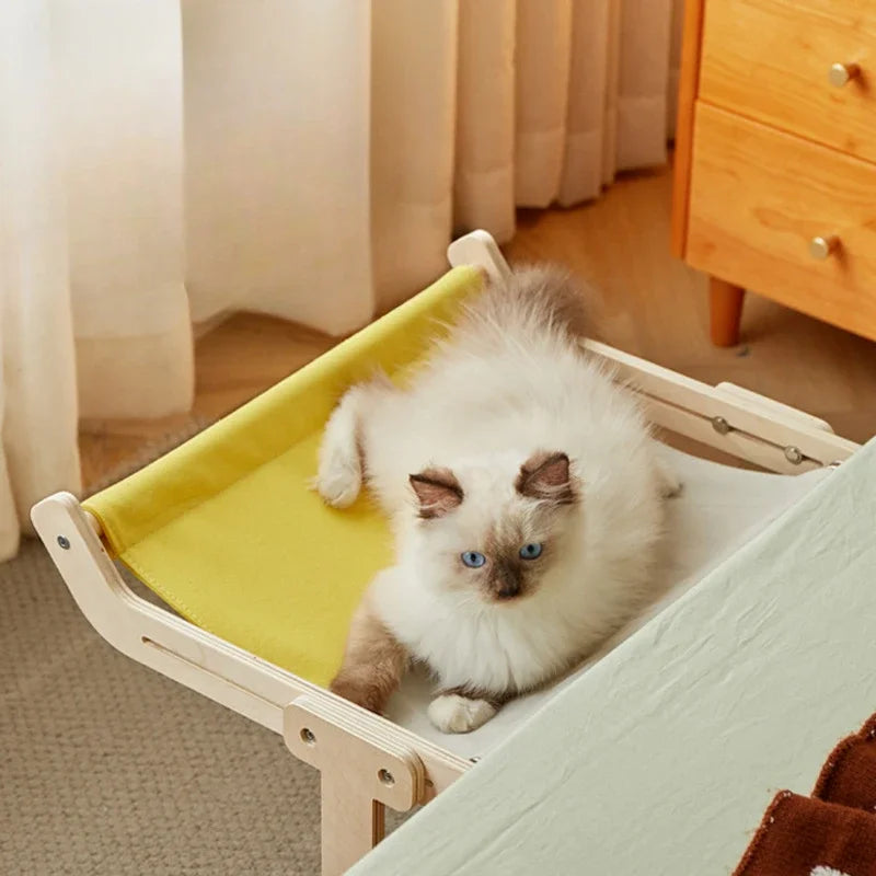 Fluffy cat lying on yellow fabric pet hammock attached to bed frame.