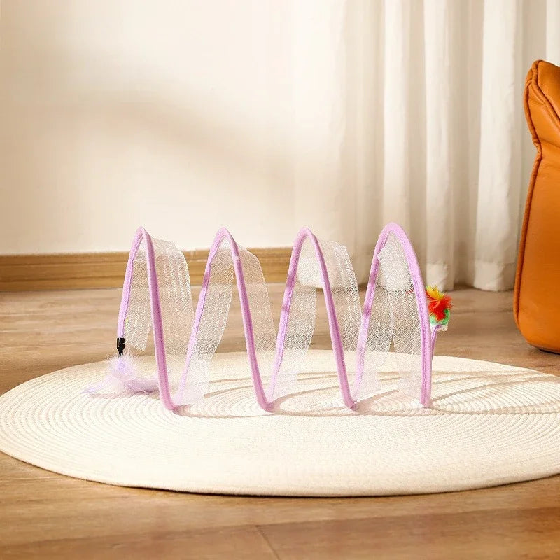 Pink and clear cat play tunnel on a wooden floor with a white curtain in the background