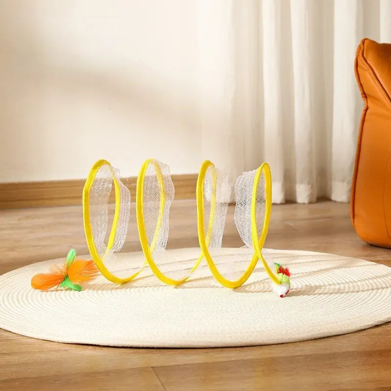 A yellow-trimmed spring-like cat tunnel with a dangling toy feather, placed on a circular mat.
