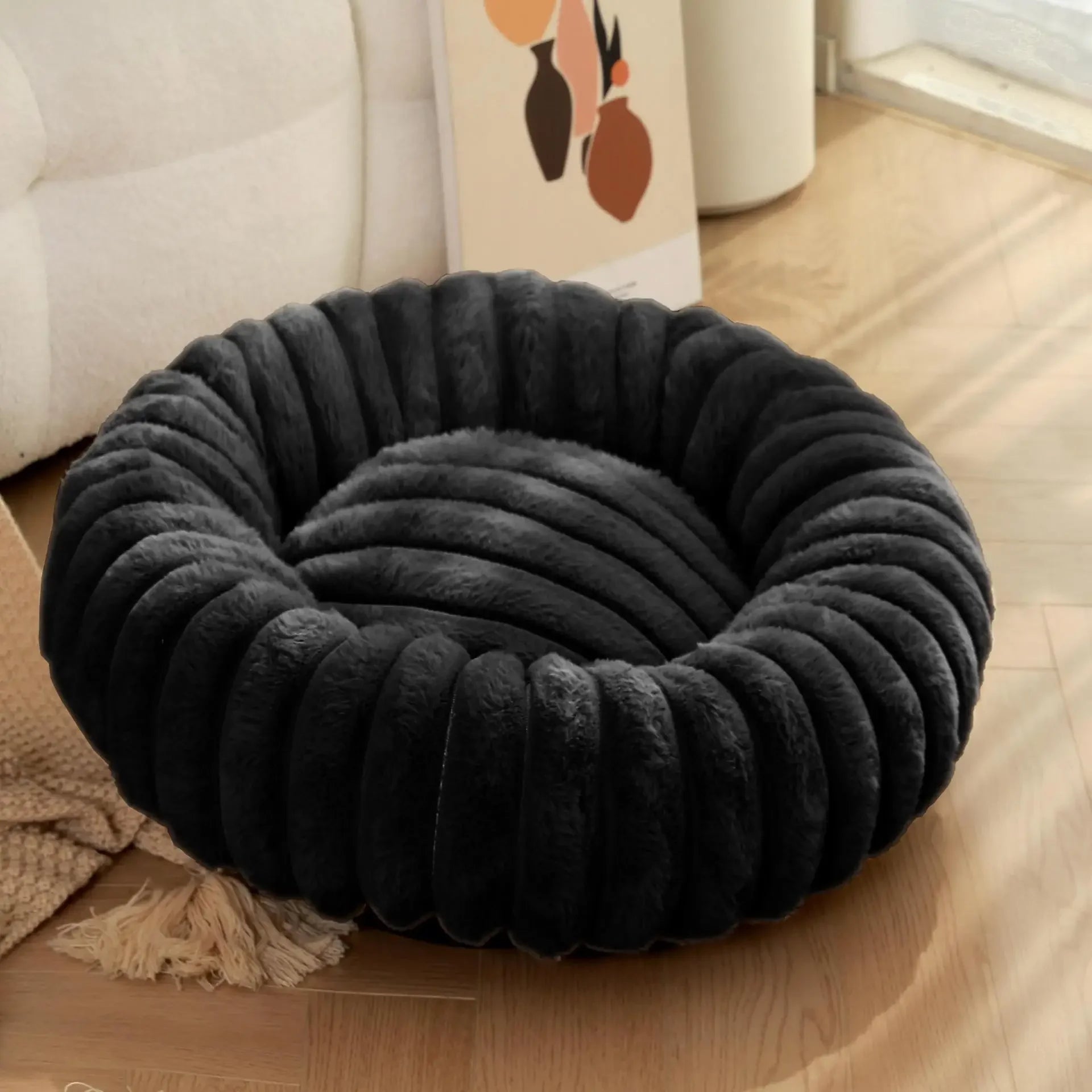 Black pet bed on a wooden floor with a blurred background