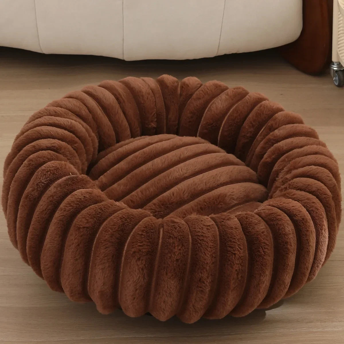 Brown ribbed pet bed on a wooden floor with a beige sofa in the background