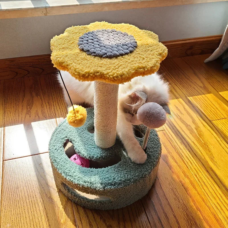 A kitten playing with pom-pom toys on a sunflower-shaped cat scratching post, reaching into the base holes.