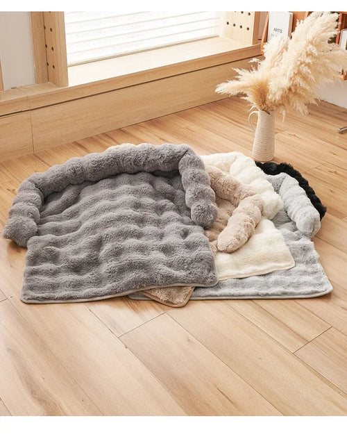 Fluffy pet bed on a wooden floor with a vase of dried plants in the background