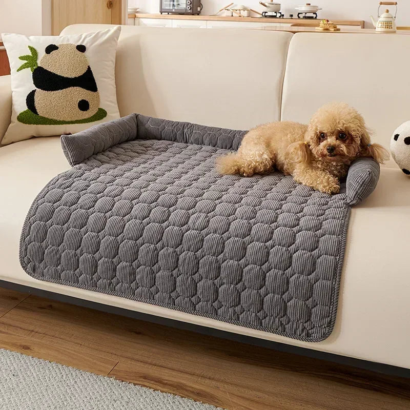 Dog lying on a gray corduroy pet bed on a white couch with a panda pillow in the background.