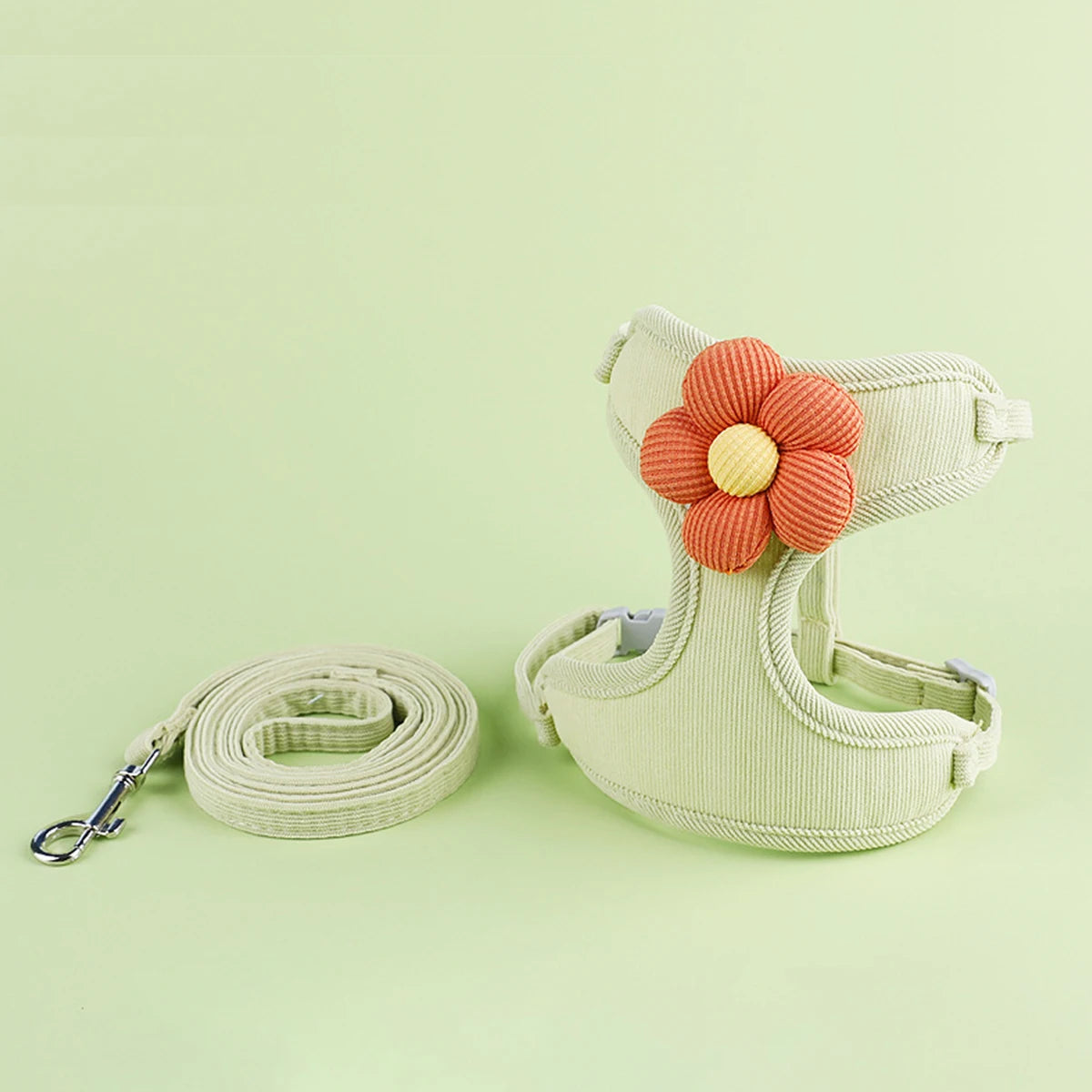 Green padded pet harness with orange flower decoration and matching leash set.