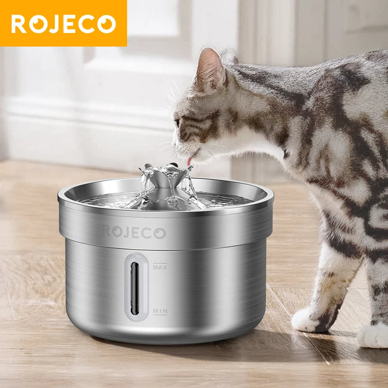 Cat drinking water from a ROJECO pet fountain on a wooden floor.