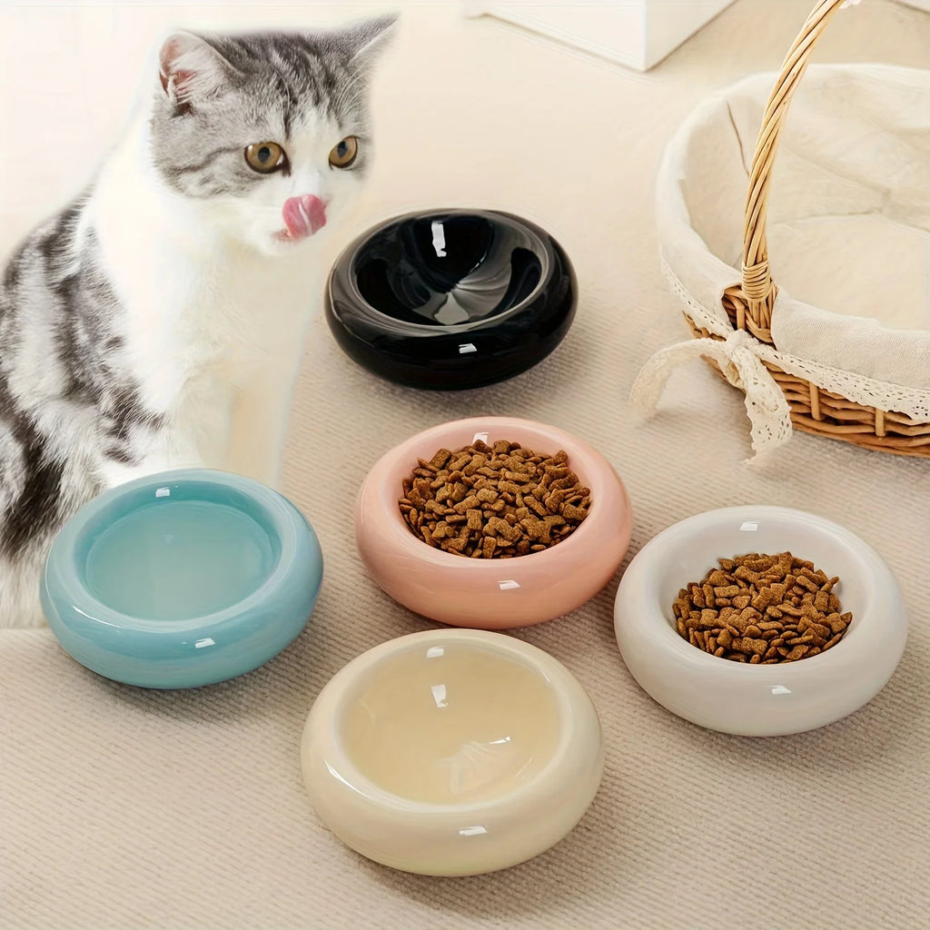 Cat sitting next to colorful ceramic bowls on a beige surface