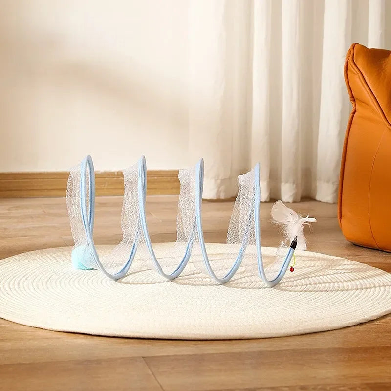 A transparent cat tunnel with light blue trim and attached toy feather, stretched on a round mat.
