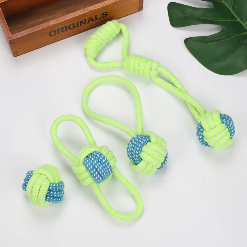 Set of four neon green and blue rope dog toys with loops and knots, placed on a table with a wooden box and green leaf decoration.