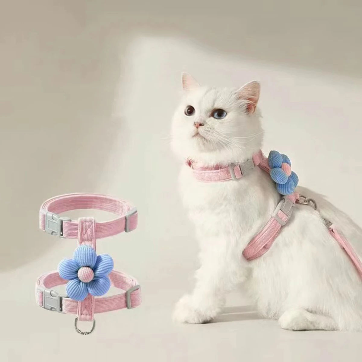 White cat modeling L-shape pink pet harness with blue flower decoration and matching leash.