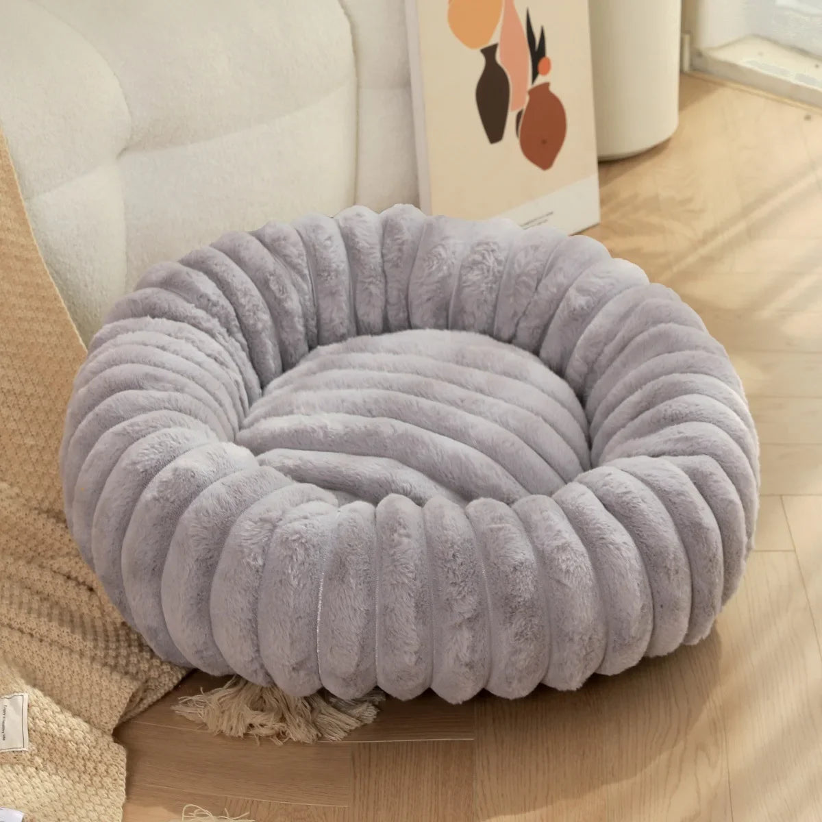 Gray pet bed on a wooden floor with a beige couch and decorative pillow in the background.