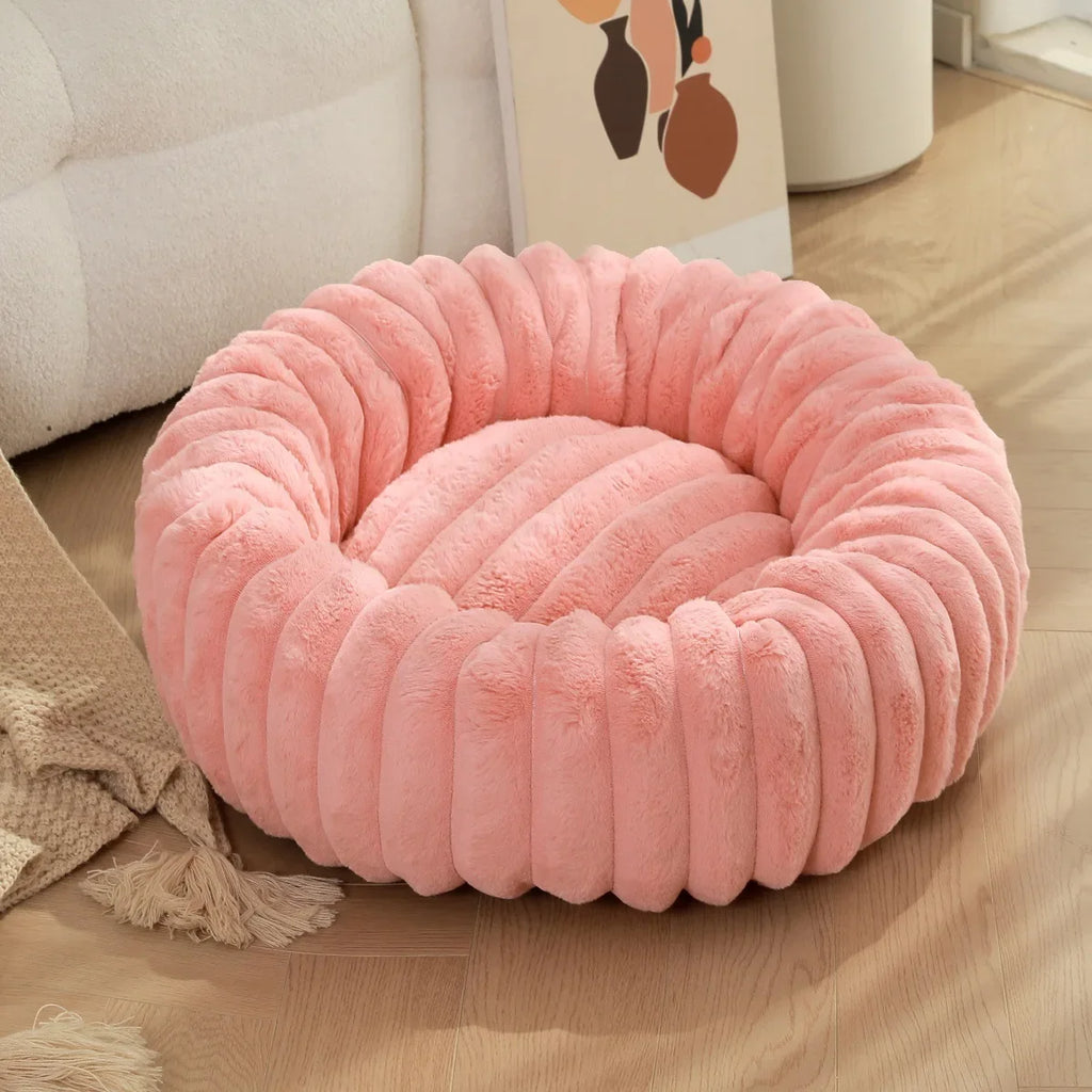 Pink plush pet bed on a wooden floor with a beige couch in the background
